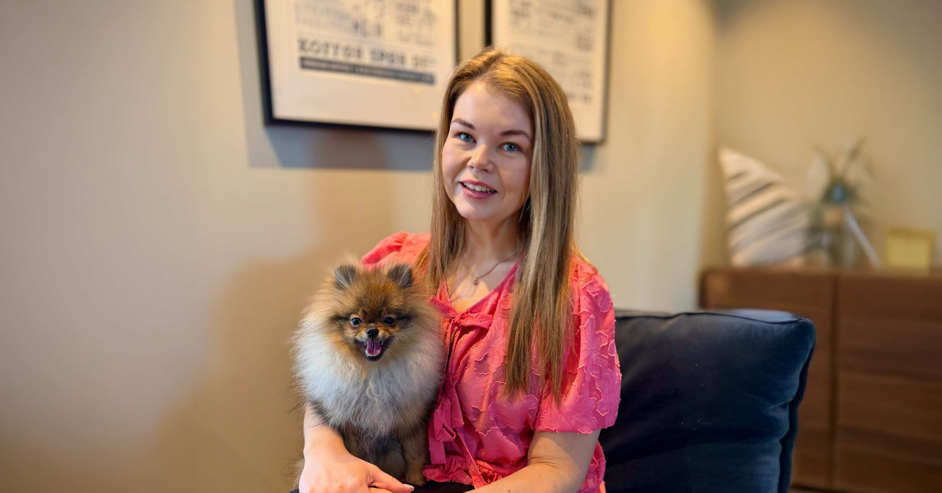 Kvinne i lyse klær smiler mot kamera med hund på fanget.