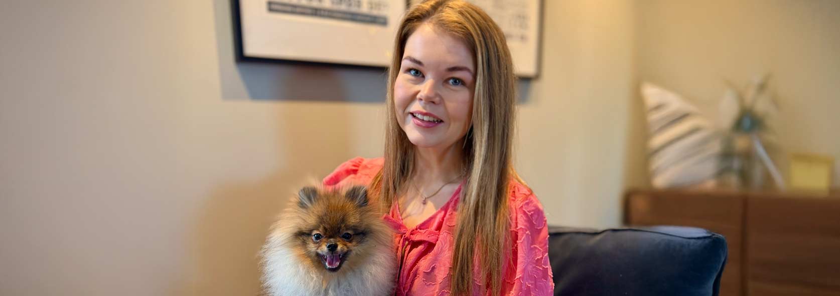 Kvinne i lyse klær smiler mot kamera med hund på fanget.